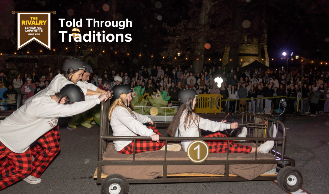 A team of students, all wearing white shirts with red and black plaid pajama pants, race their bed in front of onlookers