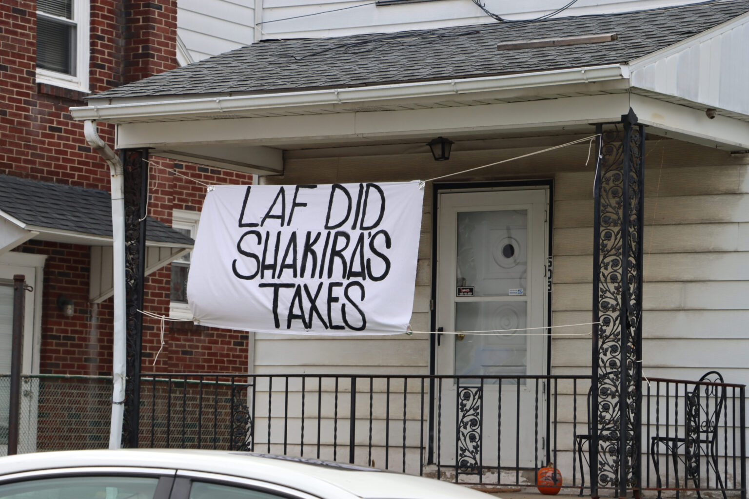 A banner reading "Laf did Shakira's taxes" hangs from the front porch of a white house. 